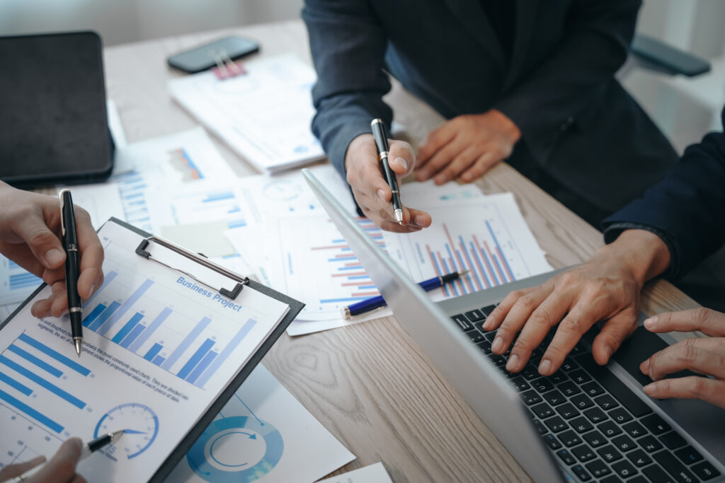A professional business team meeting in formal suits, working at desks with financial papers, calculators, and laptops. Close-up of hands. Discussion on revenue, brand, sales, agenda, capital